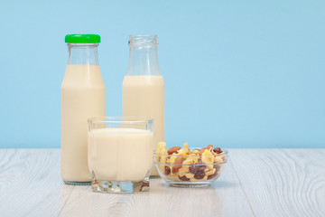 Two bottles and glass of milk, bowl with muesli on blue background.