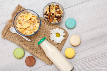 Glass bottle of milk, bowls with muesli and cornflakes on gray background