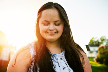 A Portrait of trisomie 21 adult girl outside at sunset
