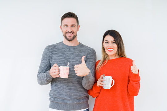 Young couple drinking cup of coffee over isolated background happy with big smile doing ok sign, thumb up with fingers, excellent sign