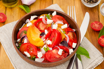 Fresh organic tomato salad with marinated onions, feta cheese and olive oil in a bowl. Rustic style.