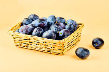 Plums in basket isolated on beige background