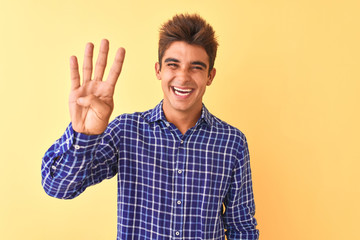 Young handsome man wearing casual shirt standing over isolated yellow background showing and pointing up with fingers number four while smiling confident and happy.