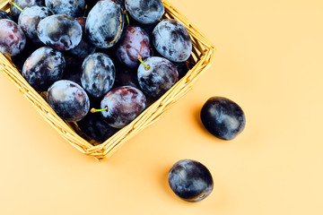 Plums in basket isolated on beige background