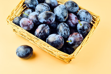 Plums in basket isolated on beige background