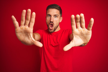 Young handsome man wearing casual t-shirt over red isolated background doing stop gesture with hands palms, angry and frustration expression