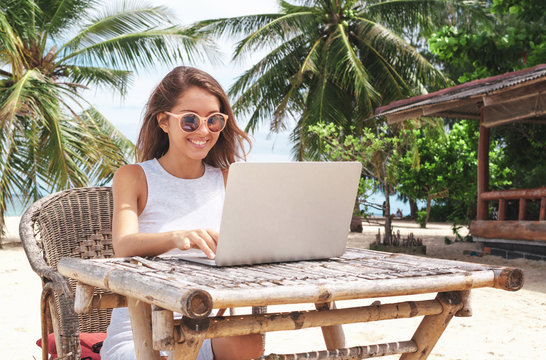 Young woman working with laptop computer on tropical island beach under palm trees Freelance  concept