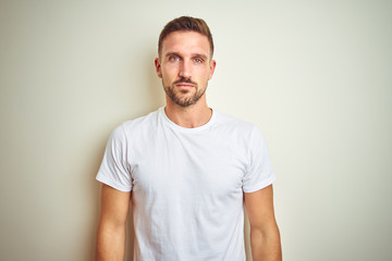Young handsome man wearing casual white t-shirt over isolated background with serious expression on face. Simple and natural looking at the camera.