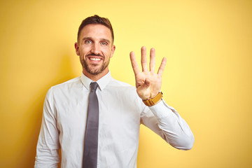 Young handsome business man wearing elegant white shirt over yellow isolated background showing and pointing up with fingers number four while smiling confident and happy.