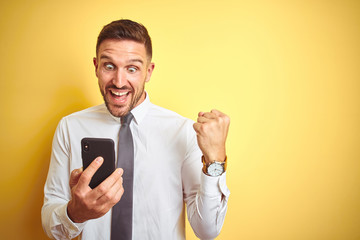 Young handsome business man using smartphone over yellow isolated background screaming proud and...