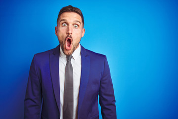 Young handsome business man over blue isolated background afraid and shocked with surprise expression, fear and excited face.