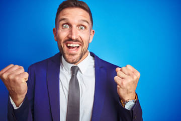 Close up picture of young handsome business man over blue isolated background celebrating surprised and amazed for success with arms raised and open eyes. Winner concept.