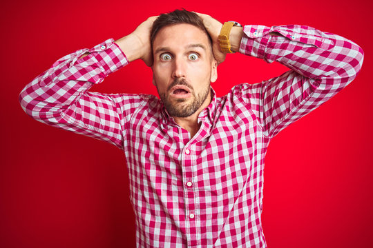 Young handsome man over red isolated background Crazy and scared with hands on head, afraid and surprised of shock with open mouth