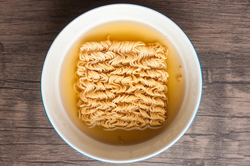Dry instant noodle and boil water in the white bowl put on wood table,