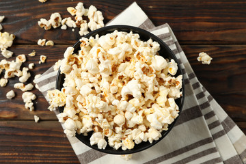 Towel and bowl with popcorn on wooden background, top view