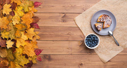 Seasonal autumn background. Frame of maple leaves and a cake and berries over wooden background.