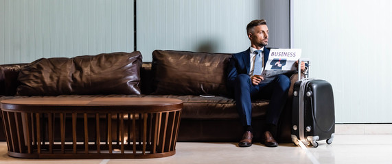 panoramic shot of handsome businessman in suit holding newspaper