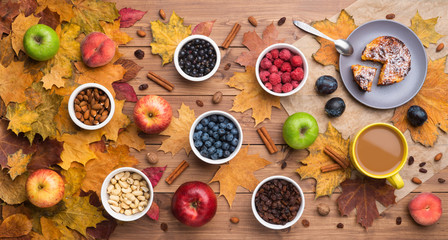 Seasonal autumn background. Frame of maple leaves and a cake, berries, raisins, apples, fruits, coffee and nuts over wooden background.
