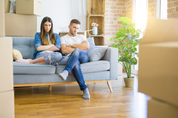 Young beautiful couple relaxing sitting on the sofa around boxes from moving to new house skeptic...