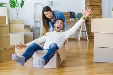 Young couple moving to a new home, having fun riding cardboard boxes