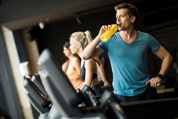 Young man drinking bottle of water on threadmill in gym