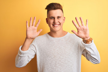 Naklejka premium Young handsome man wearing white casual t-shirt standing over isolated yellow background showing and pointing up with fingers number ten while smiling confident and happy.