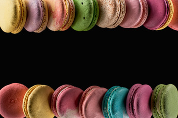 rows of delicious colorful French macaroons of different flavors isolated on black with copy space