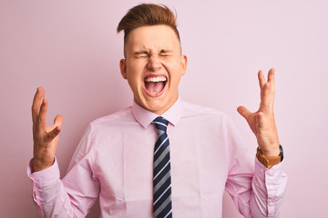 Young handsome businessman wearing shirt and tie standing over isolated pink background celebrating mad and crazy for success with arms raised and closed eyes screaming excited. Winner concept
