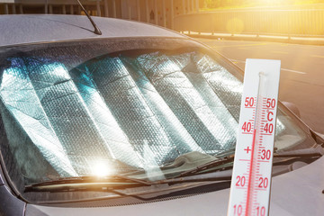 Protective reflective surface under the windshield of the passenger car parked on a hot day, heated by the sun's rays. The thermometer shows the temperature inside the car.