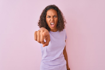 Young brazilian woman wearing t-shirt standing over isolated pink background pointing displeased and frustrated to the camera, angry and furious with you