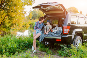 mother woman and child son comfortably relax in nature by the river sitting on the trunk of a jeep.