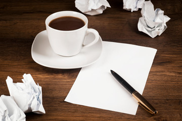 A cup of coffee, a sheet of paper with a pen and crumpled sheets of paper on the counter from the desk