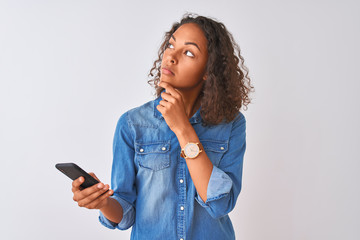 Young brazilian woman using smartphone standing over isolated white background serious face...