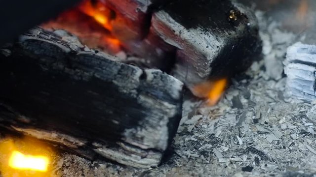 burning black coals close-up. The wind blows away flakes of gray ash and smoke. The edge of the wood burns with a small flame.