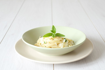 dish of spaghetti with spring onion and mint in an elegant wooden table