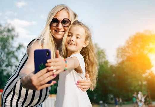 Image of happy mother and daughter taking selfie on street on summer day