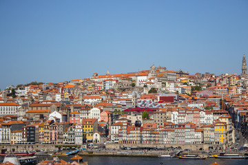 Fototapeta na wymiar River Douro with colorful embankment of Porto. Porto panoramic landmark with boats on sunny day. Old buildings with brick roofs by river Douro in Porto, Portugal. Historic district of Porto. 