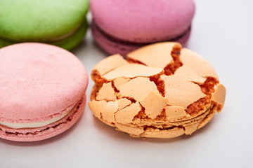 close up view of sweet colorful French macaroons of different flavors with smashed one on white background