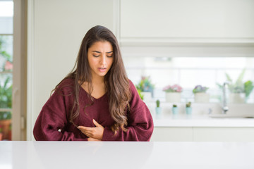 Young beautiful woman at home with hand on stomach because indigestion, painful illness feeling...