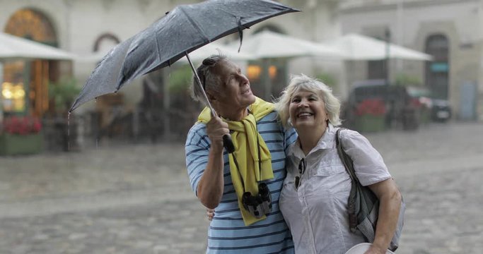 Happy senior tourists stand downtown and enjoy the rainy weather in Lviv