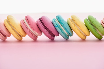 row of delicious colorful French macaroons of different flavors on pink background with copy space