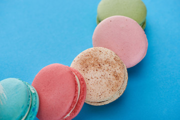 close up view of multicolored tasty French macaroons on blue bright background