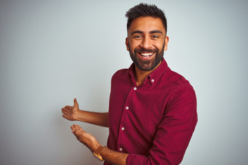 Young indian man wearing red elegant shirt standing over isolated grey background Inviting to enter...