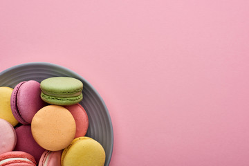 close up view of plate with multicolored delicious French macaroons on pink background