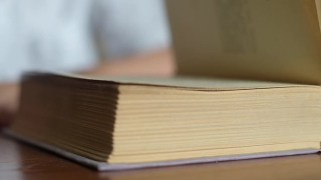 the student quickly turns the pages of a large book lying on a wooden table and closes the cover of literature. Close-up, angle view