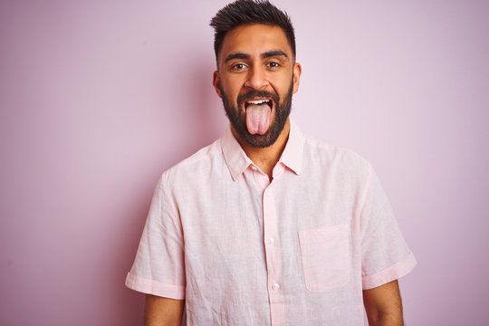 Young indian man wearing casual shirt standing over isolated pink background sticking tongue out happy with funny expression. Emotion concept.