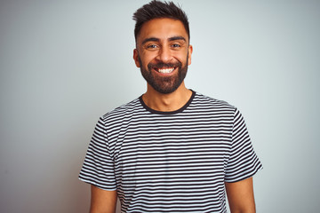 Young indian man wearing black striped t-shirt standing over isolated white background with a happy and cool smile on face. Lucky person.