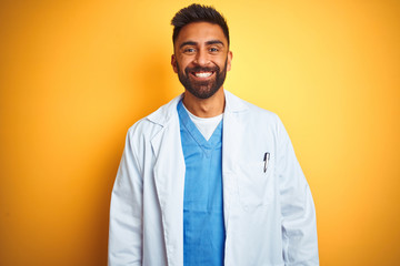 Young indian doctor man standing over isolated yellow background with a happy and cool smile on...
