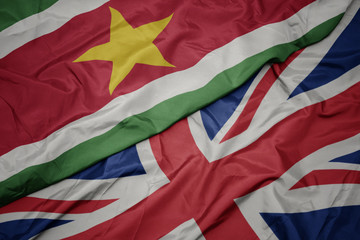 waving colorful flag of great britain and national flag of suriname.