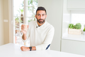 Fototapeta premium Handsome hispanic man drinking a coffee in a paper cup with a confident expression on smart face thinking serious
